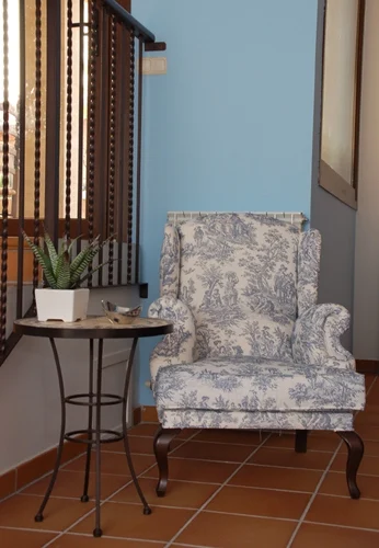 Sillón tapizado junto a una ventana y una mesa de forja